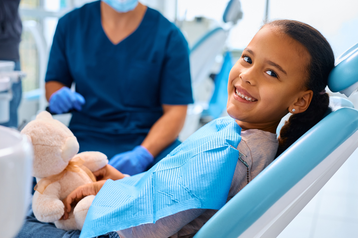Child holding a teddy bear and smiling during a dental visit