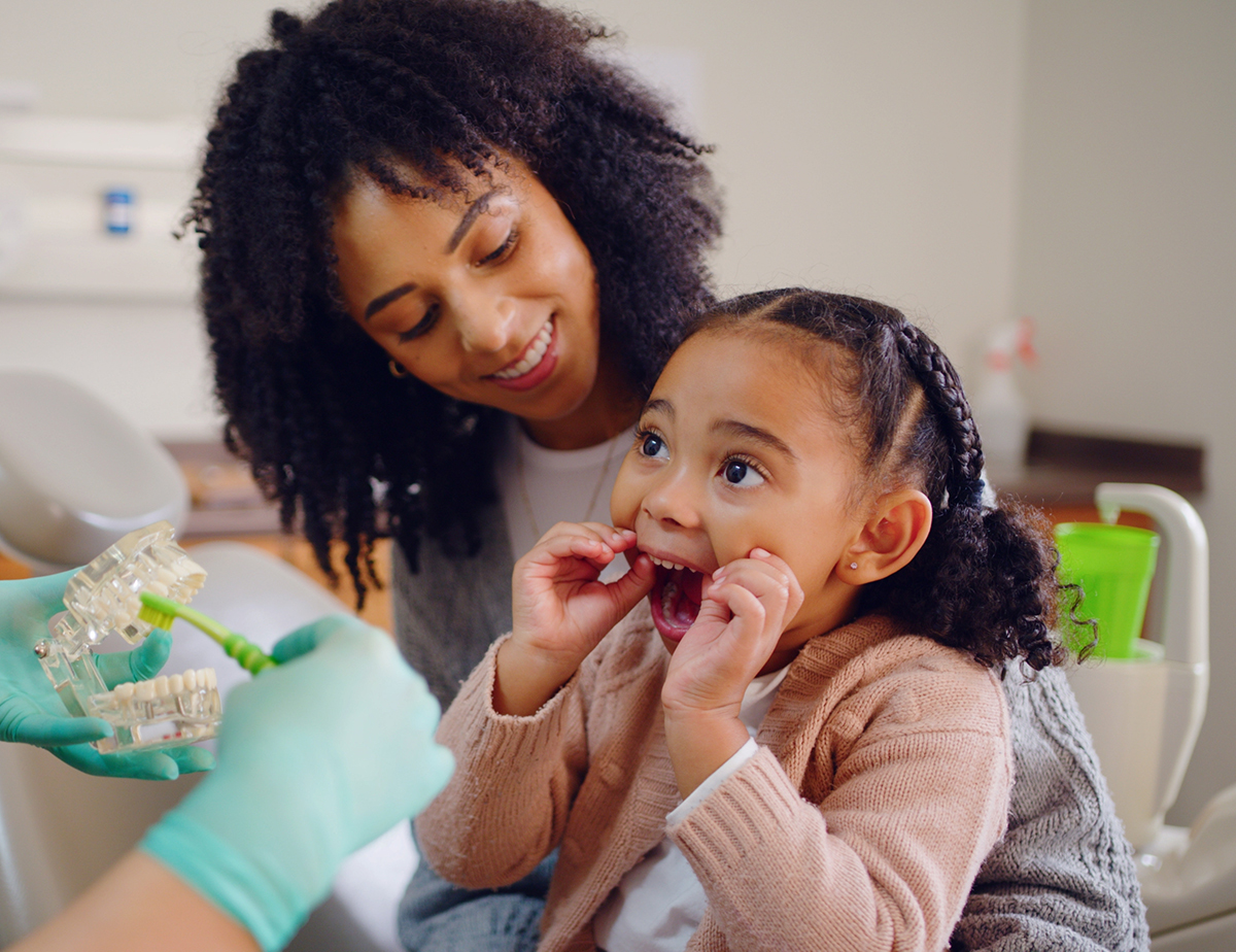 Pediatric dentist showing a child and parent a model of teeth and how to brush